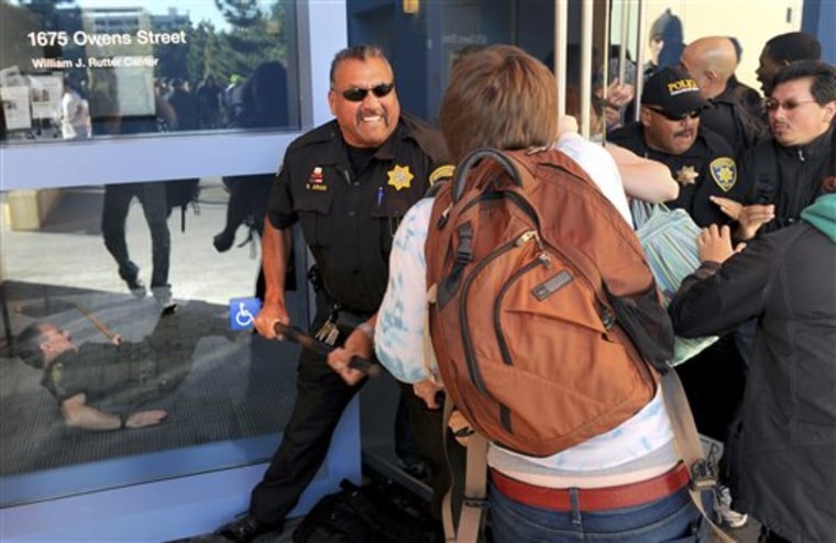 A police officer uses a baton to fend off protesters attempting to enter a University of California regents meeting on Wednesday in San Francisco. 